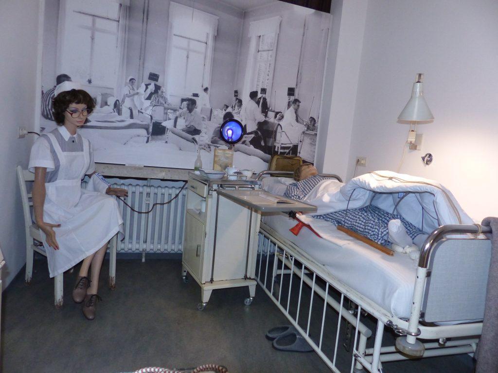 Historisches Krankenzimmer mit einem Patientenbett und einer Pflegeszene im Krankenhausmuseum
